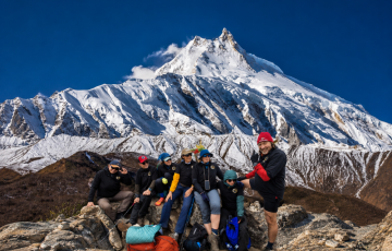 Group of trekkers posing on rocky terrain below the majestic snow-covered Manaslu peak near Larke Pass, with the summit rising clearly against a deep blue Himalayan sky. Group of trekkers posing on rocky terrain below the majestic snow-covered Manaslu peak near Larke Pass, with the summit rising clearly against a deep blue Himalayan sky.