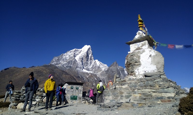 How to prepare for high altitude trekking on the Everest Base Camp trail-Trekker standing in front of snow-capped mountains at Everest base camp, surrounded by colorful prayer flags.